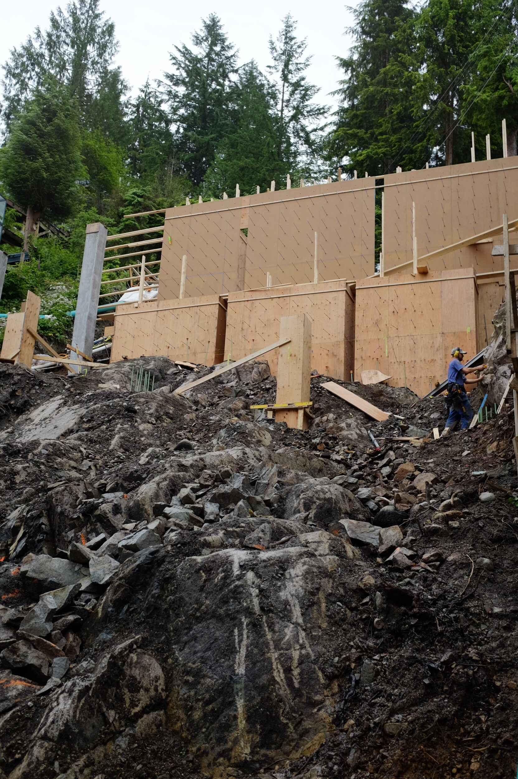 Wood framing for a home rises up from hill of mud and bedrock