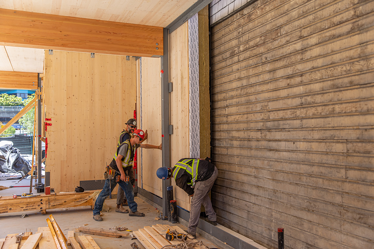 Construction crew slide wood panel into place alongside building edge