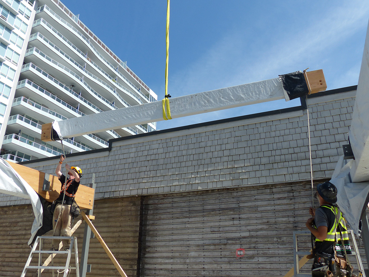 Construction team members watch as a crane hoists horizontal beam into place