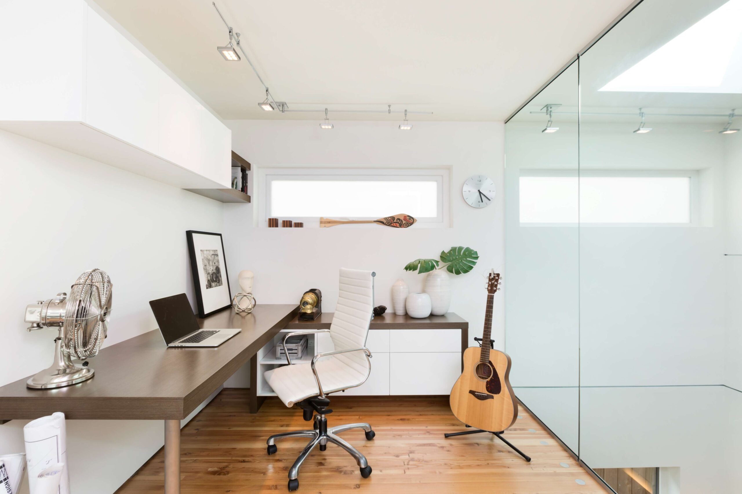 A guitar sits on a stand in a home office with glass walls