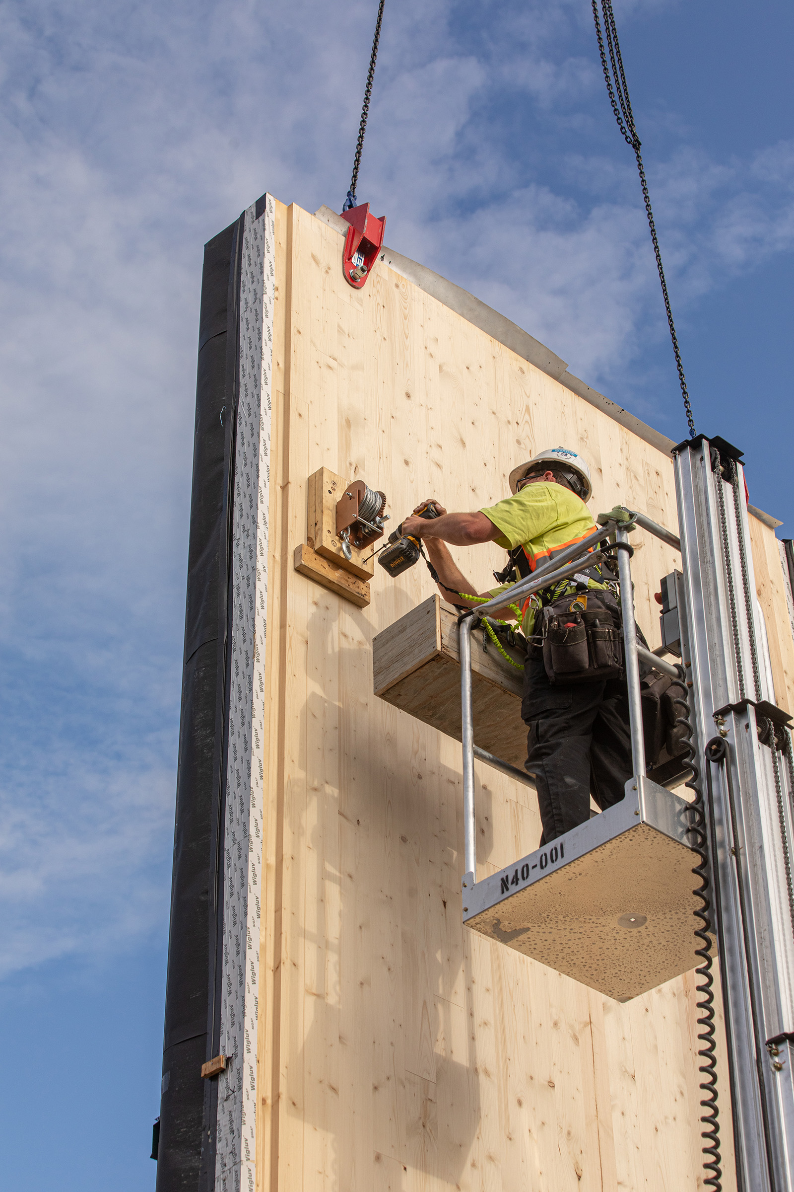 A construction worker drills into a hoisted wood panel